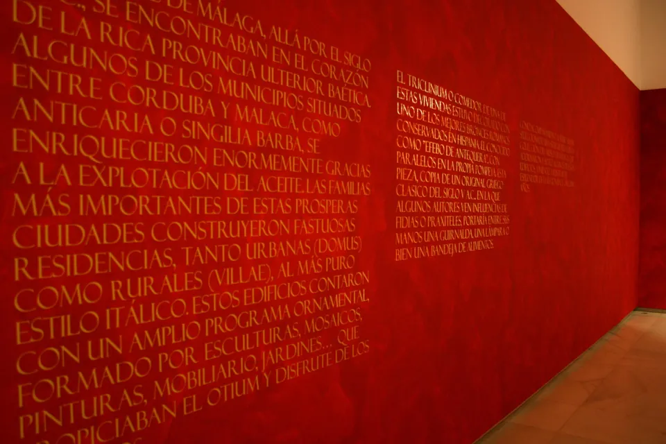Texto en vinilo sobre pared roja en la exposición del Efebo de Antequera